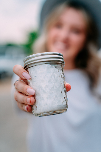 Close-Up Shot of a Young Happy Caucasian Woman Holding a Glass Mason Jar of Lavender Sugar at a Local Small Business Farm-to-Table Supplier in Colorado