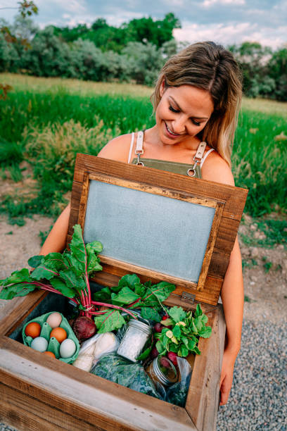 Portrait of a Young Happy Caucasian Woman Holding a Wooden Box of Delicious, Healthy, Organic Produce at a Local Small Business Farm-to-Table Supplier in Colorado retrato de una joven caucásica feliz sosteniendo una caja de madera de huevos deliciosos, saludables y orgánicos, rábanos, remolachas, azúcar y otros productos locales en un proveedor local de la granja a la mesa de una pequeña empresa en colorado