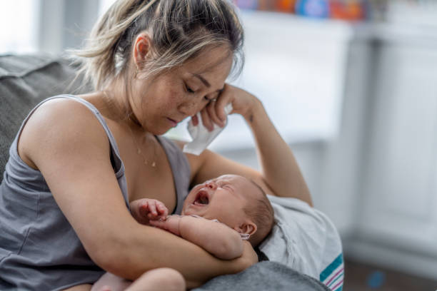 Postpartum stress A middle aged mother resting on her couch holds up her baby on her chest with a tired and stressed expression. postpartum depression stock pictures, royalty-free photos & images