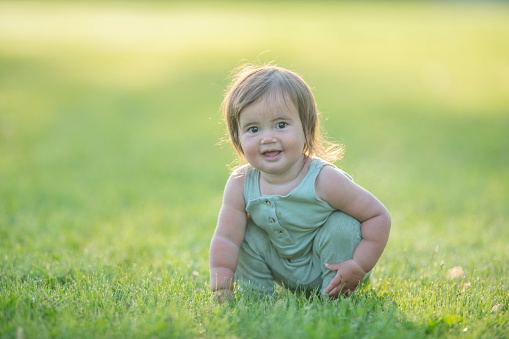 A one year old baby girl crawls in the outdoors and smiles up at the camera.