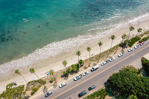 Aerial over palm-tree lined road along the Pacific Ocean