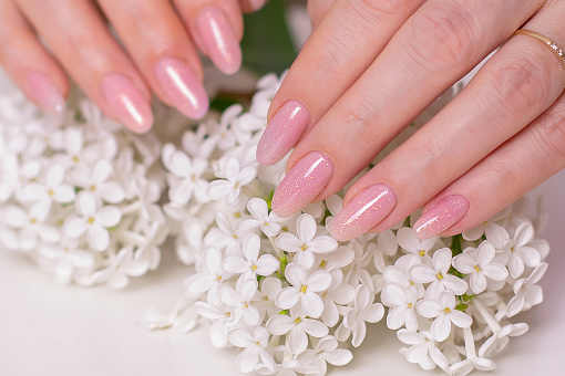 Beautiful female hands with wedding manicure nails, pink gel polish and white flowers