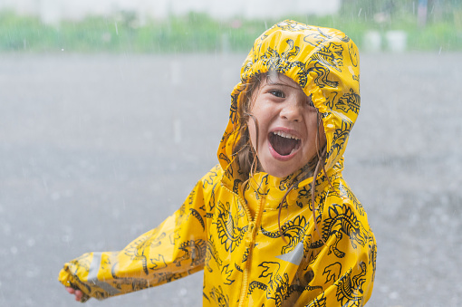 The girl wear yellow raincoat and enjoy the rains. Happy child under an summer shower.
