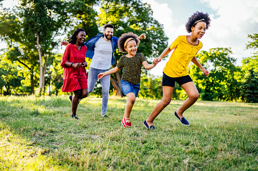 Multi-ethnic family is running outside in a grassy field - they are laughing while chasing each other