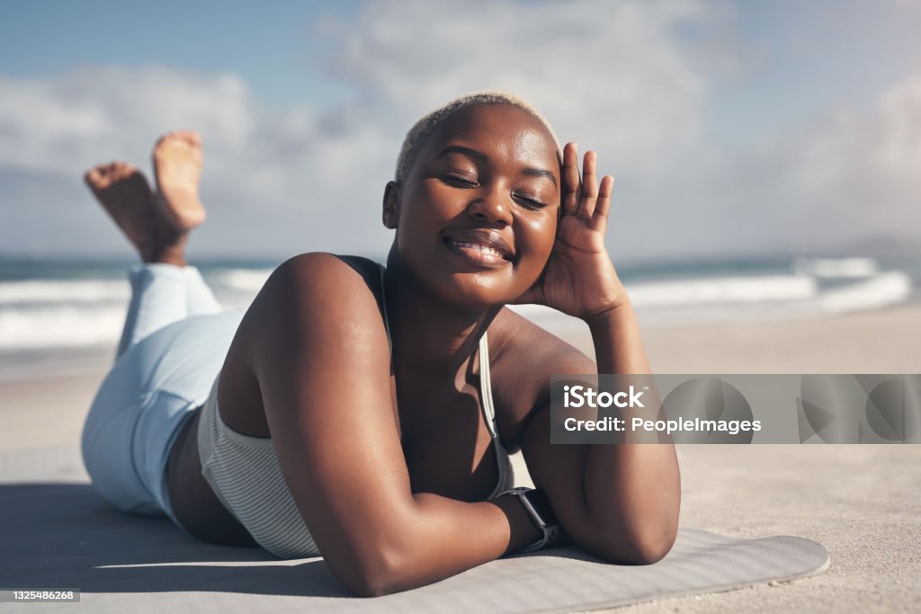 Shot of a sporty young woman lying on her yoga mat at the beach I can't imagine life without yoga now Beach Stock Photo