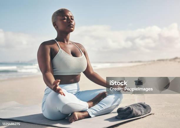 Shot of a woman meditating during her yoga routine on the beach