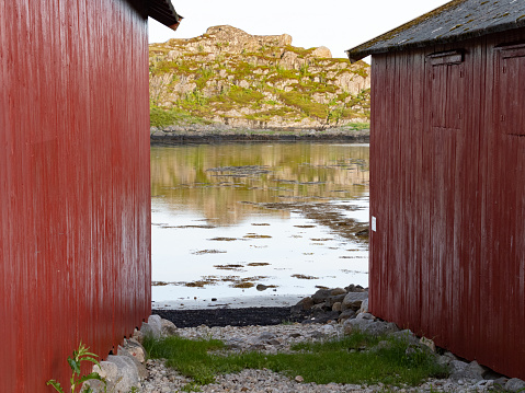 An inlet at low tide seen through two red boathouses.