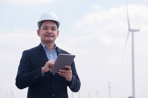 Successful engineer windmills manager standing and hoding tablet with wind turbine in background stock photo