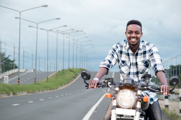 African biker man riding a motorcycle rides on highway road stock photo