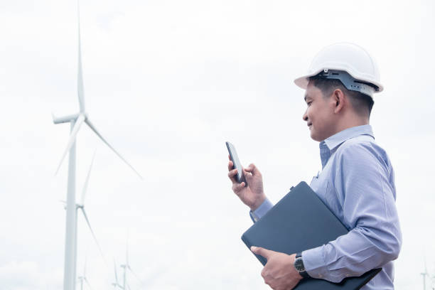 Success engineer windmills using smartphone and holding laptop with the wind turbine in background stock photo
