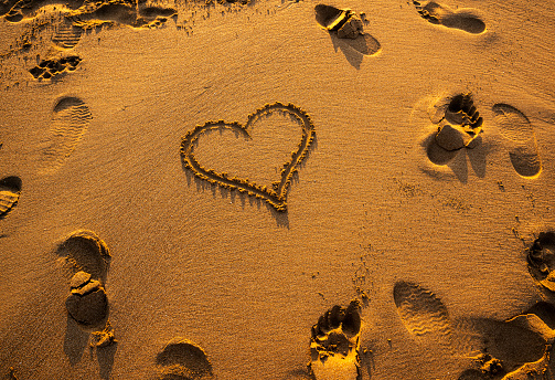 Drawing Heart Shapes on Sandy Beach with Wooden Stick at Sunset