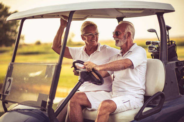 os golfistas estão andando em um carrinho de golfe. - senior couple golf retirement action - fotografias e filmes do acervo
