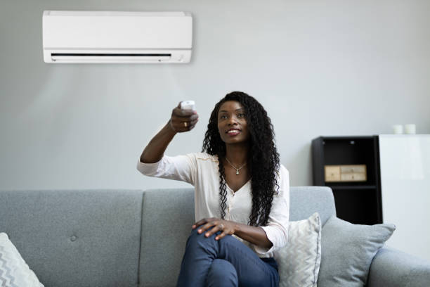 istock Woman Sitting On Couch Operating Air Conditioner 1325532590