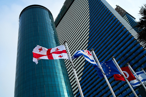 Flags of countries on flagpoles against the backdrop of modern skyscrapers.