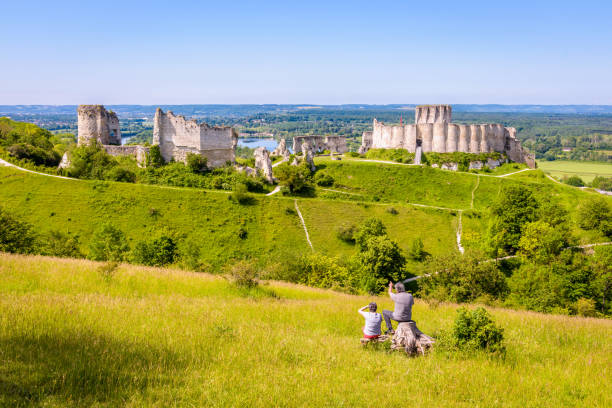 A retired couple watching the ruins of Château-Gaillard medieval fortified castle in Normandy. Les Andelys, France - June 6, 2021: A retired couple sitting on a stump is watching the ruins of Château-Gaillard, a fortified castle built in Normandy by Richard the Lionheart in the 12th century. bailey castle stock pictures, royalty-free photos & images