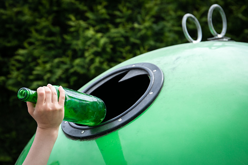 Child's hand throws the glass bottle in a green container