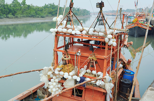 Fraserganj Fishing harbour, West Bengal, 01-24-2021: Traditional fishing trawlers docked along bank of Edward Creek. Fishing nets, nylon ropes, inflatable white plastic balls etc. are seen on boats.