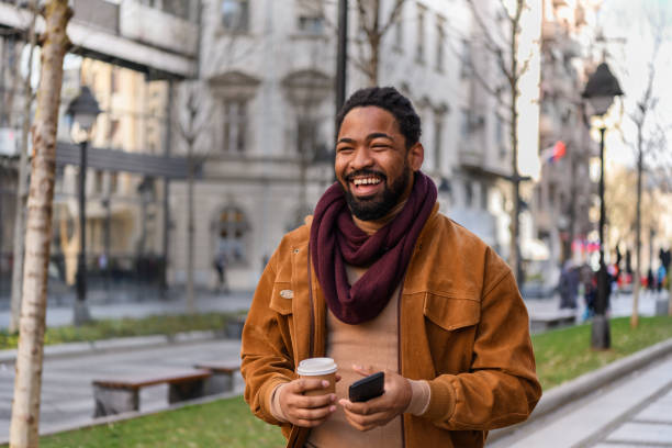 retrato de un hombre africano guapo con café caminando por las calles de la ciudad. - contemporary elegance telephone urban scene fotografías e imágenes de stock