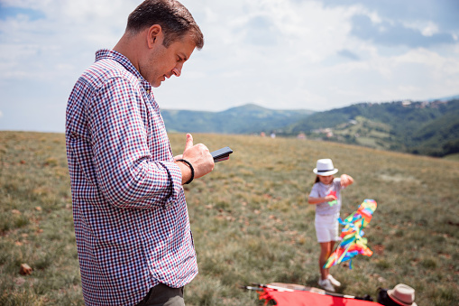 Serious man looking at his smart phone as his daughter plays outdoors