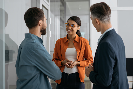 Confident African American woman explaining something, communication with business colleagues in office. Group of multiracial business people working together, talking, discussion start up