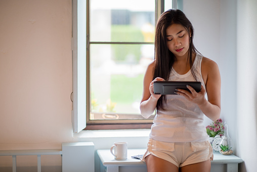 Asian woman standing and using tablet at home.