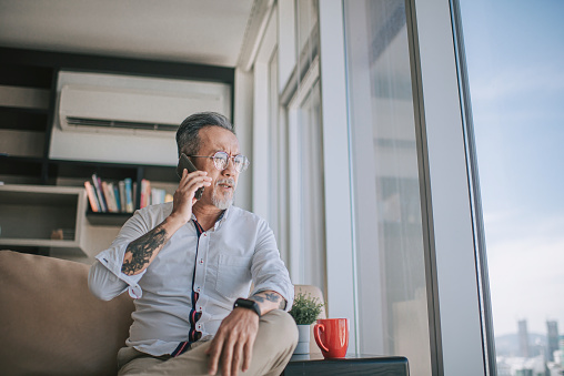 worried sad asian chinese senior man arguing on the phone at living room sitting on sofa during day time