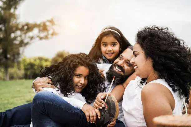 Photo of Happy indian family having fun at city park painting and laughing together - Parents and children enjoying summer day outdoor - Love concept - Focus on kid face