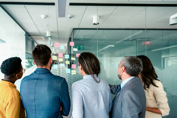 istock Serious multiethnic colleagues in formal wear developing work plan and goals in creative corporate office by writing and sticking papers with charts on glass wall 1325584223