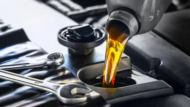 Photo of Pouring motor oil for motor vehicles from a gray bottle into the engine