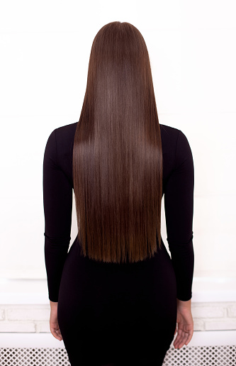 Female back with long straight brunette hair in hairdressing salon
