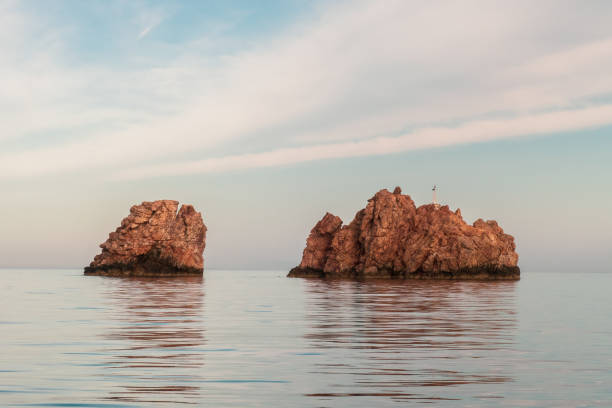 rocas que sobresalen de la superficie plana del agua de mar. - nes fotografías e imágenes de stock