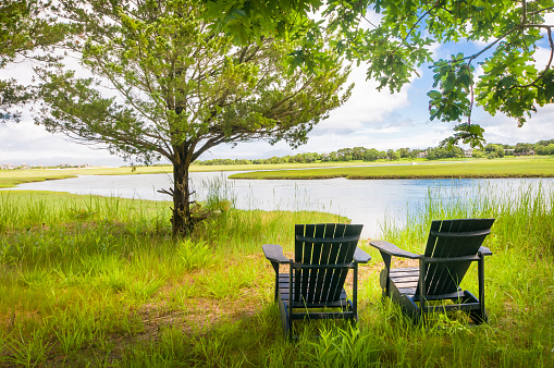 Two Adirondack chairs rest along side a tidal river on Cape Cod on a beautiful early summer day.