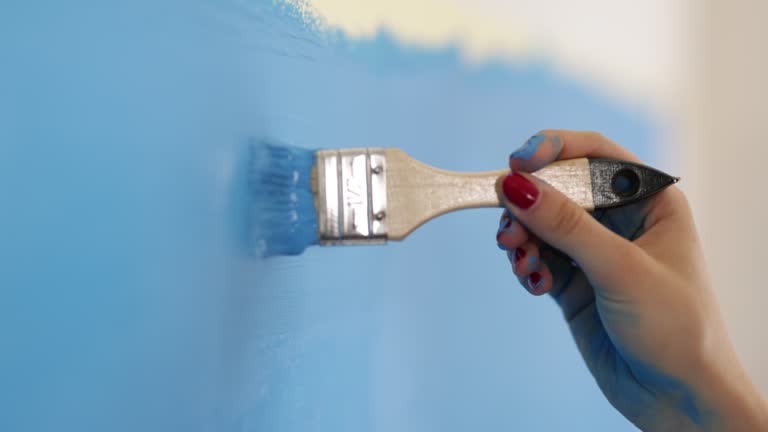 Teenage girl painting the wall with blue paint