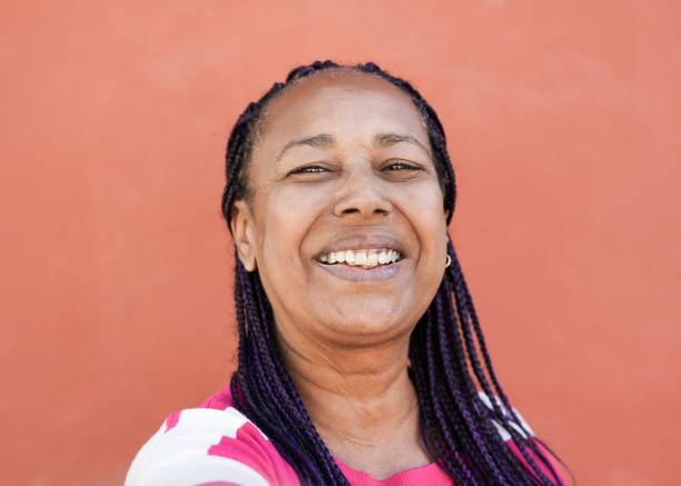Cool elderly african woman with braids taking a selfie while smiling in camera - Trendy senior african american person in the city with red background
