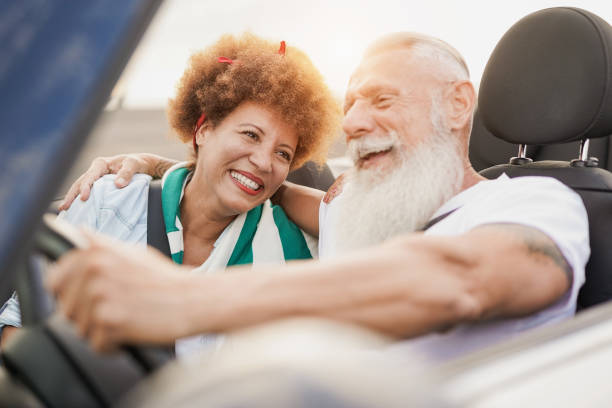 pareja madura de moda divirtiéndose dentro de un coche convertible - personas mayores multirraciales en un viaje por carretera con coche descapotable - upper class wealth women senior adult fotografías e imágenes de stock