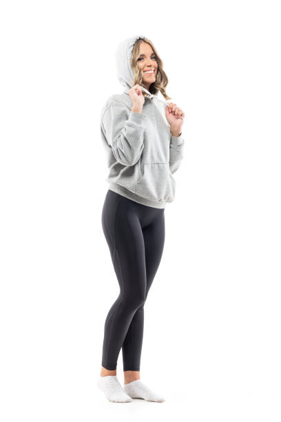 Side view of happy beauty woman in leggings put on hoodie in gray sweatshirt. Side view of happy beauty woman in leggings put on hoodie in gray sweatshirt. Full body length isolated on white background. woman putting on socks stock pictures, royalty-free photos & images