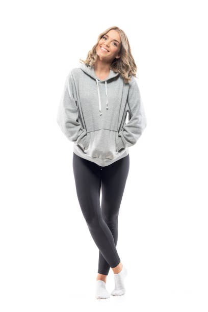 Happy relaxed young woman in hooded sweatshirt smiling and posing with hands in pockets Happy relaxed young woman in hooded sweatshirt smiling and posing with hands in pockets. Full body length isolated on white background. full body isolated stock pictures, royalty-free photos & images