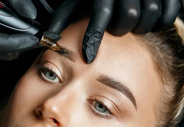 Cosmetician doing eyebrow tattooing on a female brows. Closeup shot