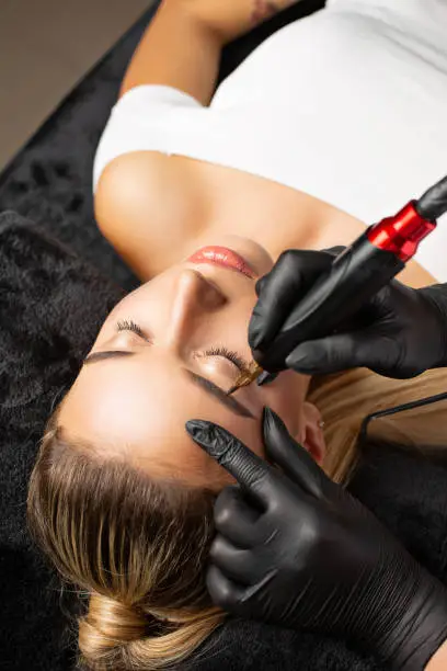 Woman in gloves making permanent brow makeup to a pretty blonde woman in cosmetology salon. Top view