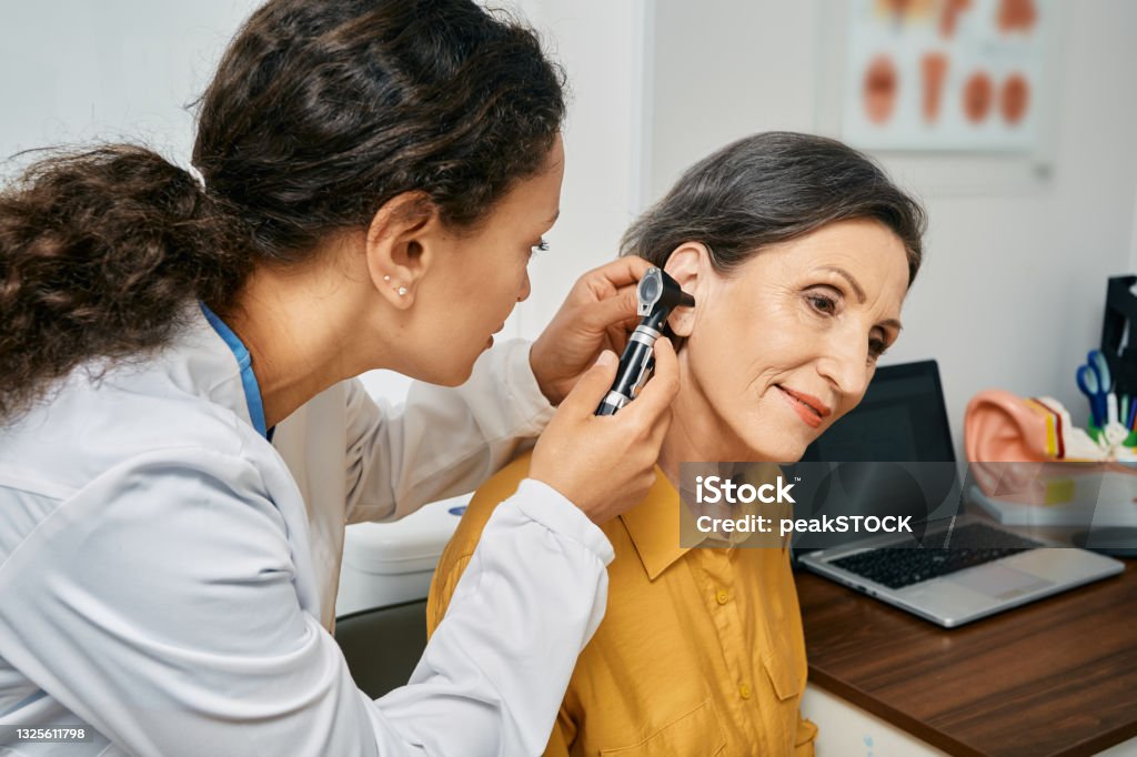 Hearing exam for elderly citizen people. Otolaryngologist doctor checking mature woman's ear using otoscope or auriscope at medical clinic Listening Stock Photo