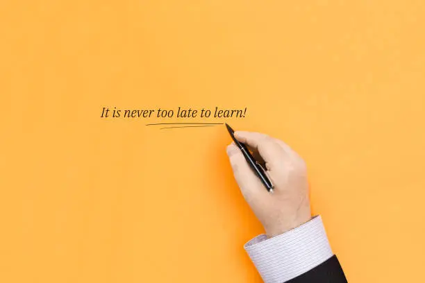 It is never too late to learn. Handwritten text on an orange background.