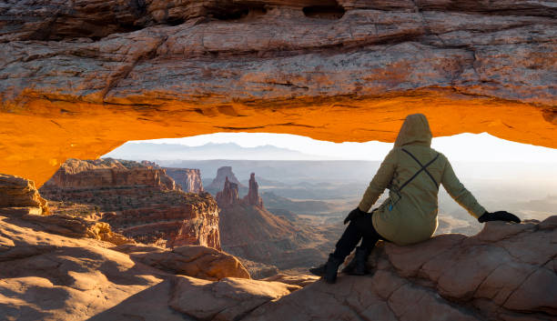 mulher olhando para mesa arch ao nascer do sol, canyonlands national park, utah, eua - canyonlands national park utah mesa arch natural arch - fotografias e filmes do acervo
