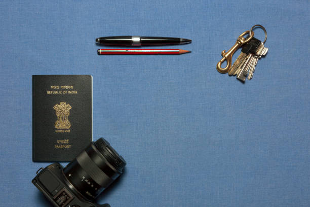 ansioso por viajar : un laico plano del nuevo pasaporte de la india, una cámara réflex digital de una sola lente, bolígrafo, lápiz y un montón de teclas que se muestran sobre un fondo azul liso que indica el deseo de viajar internacionalmente. - passport blank book cover empty fotografías e imágenes de stock