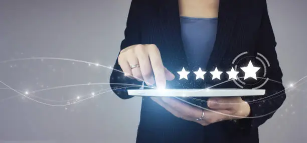 Photo of Five stars 5 rating with a hand touching screen. White tablet in businesswoman hand with digital hologram Five stars 5 rating sign on grey background.