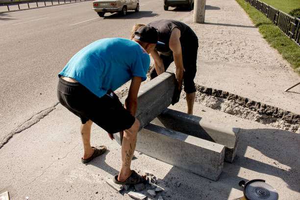 the process of laying sidewalk curb. workers place a deflected piece of concrete curb into a prepared recess or trench. - n64 imagens e fotografias de stock