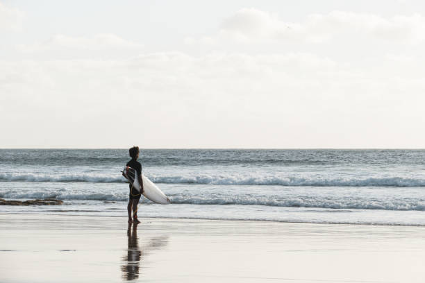 istock Surfer watching the waves standing at the beach shore at sunset 1325633418