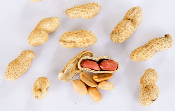istock Peanuts scattered on a white background. One was opened to reveal a red seed inside. 1325636211