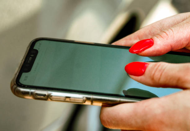 istock Female hands with red manicure on mobile phone screen 1325641557