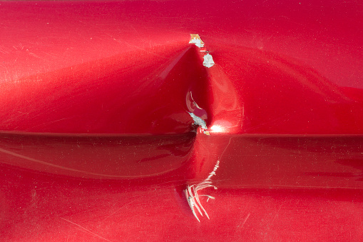 A dent in the car. The spoiled surface of the car. Spoiled painting of the car.