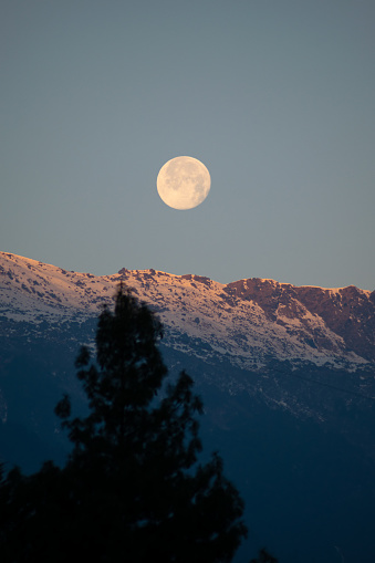 shining full moon visible while the first rays of the sun starts to fall on the snow covered himalayan mountain